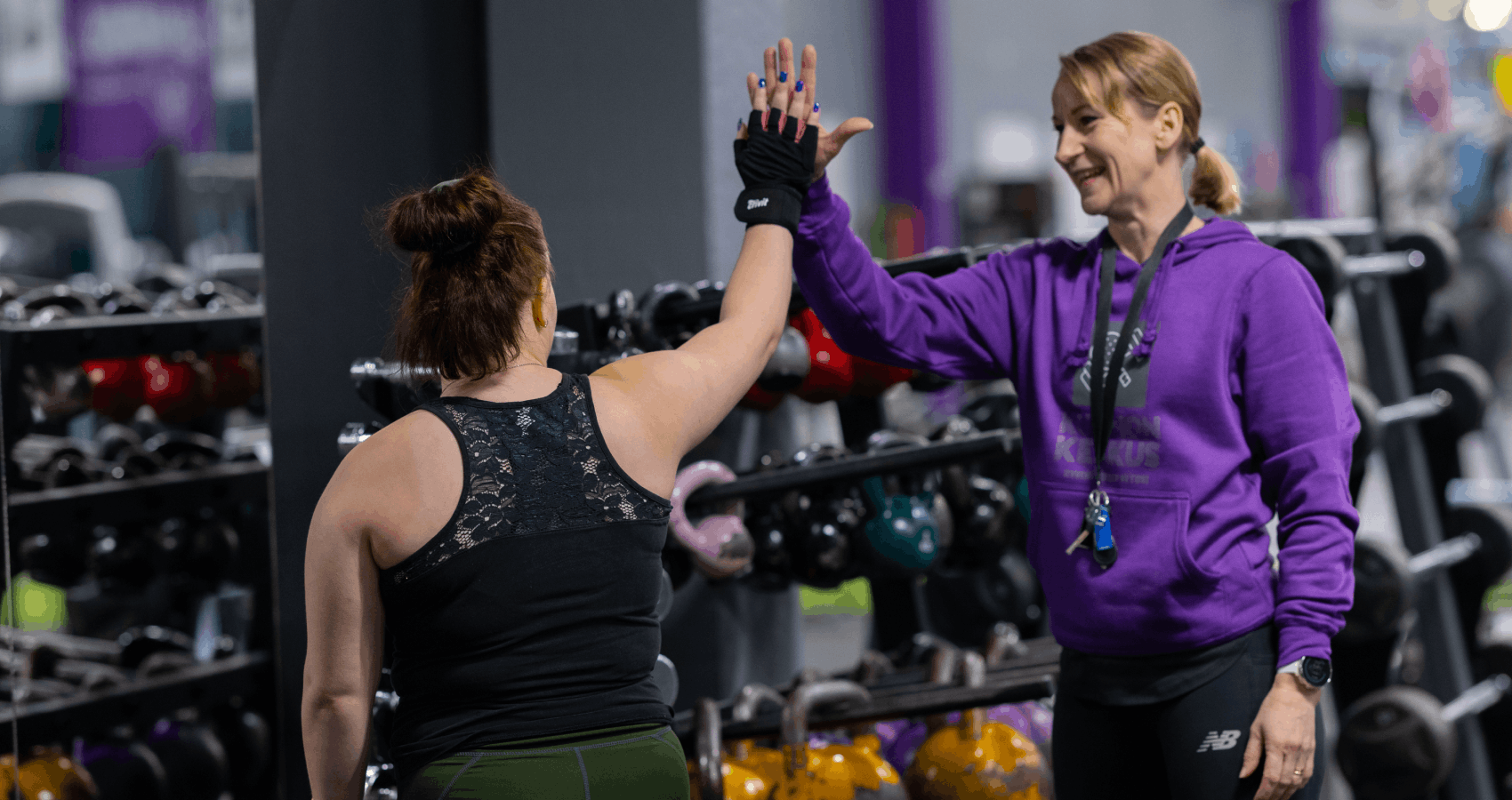 Personal trainer ja asiakas antavat ylävitosen kuntosalilla